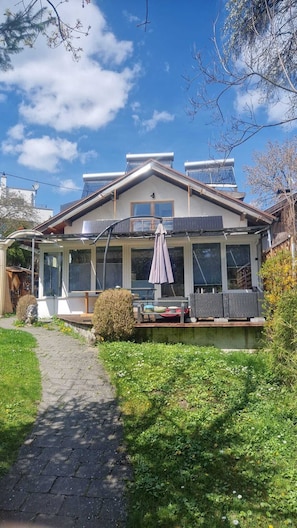 Una casa con porche cubierto, paneles solares y un sendero en el jardín.