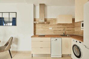 A compact kitchen with a dishwasher, washing machine, and a wooden backsplash. - ARENA SUITES SPA Apartamento con Jacuzzi (Chiclana de la Frontera)