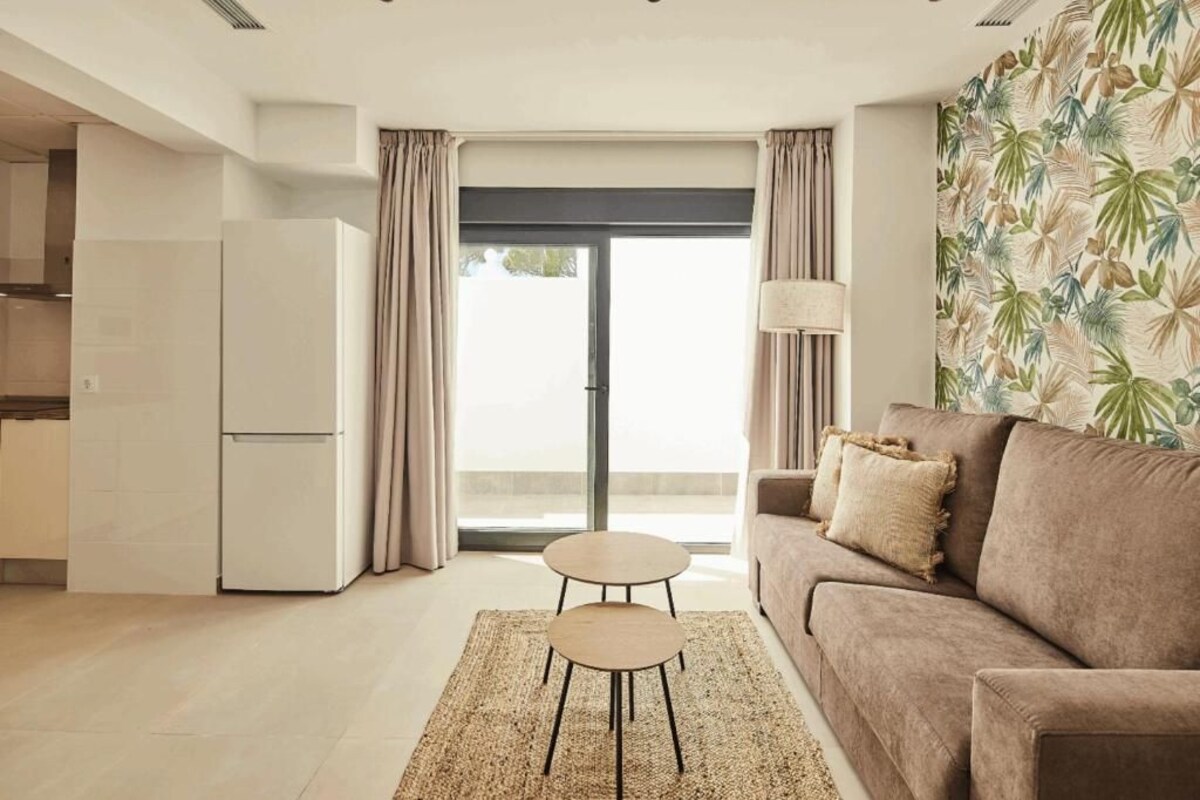 A modern living room with a sofa, a coffee table, and a kitchen area with a refrigerator.