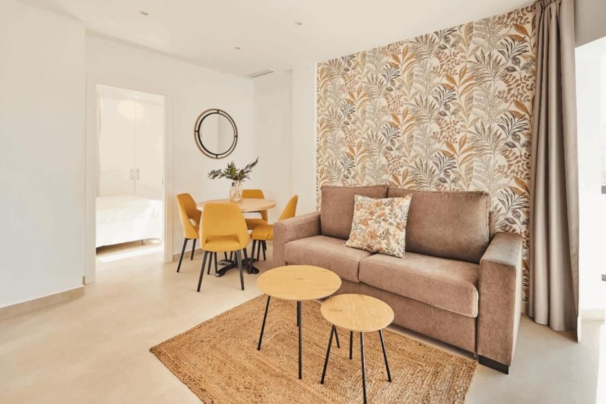 A modern living room with a sofa, two round tables, a dining table with chairs, and a decorative wall.