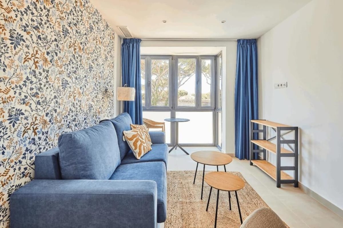 A modern living room with a sofa, two small round tables, a bookshelf, and a large window with curtains.