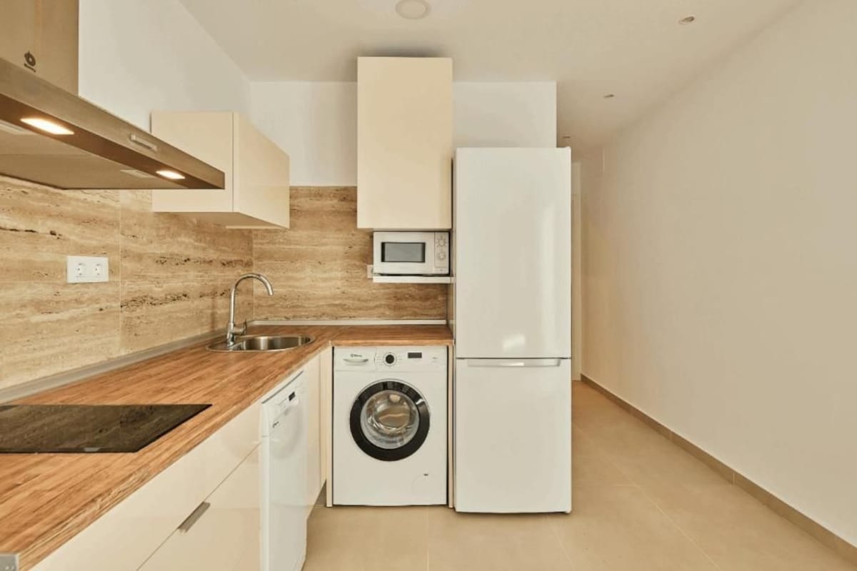 A compact kitchen with a washing machine, a microwave, and a refrigerator.