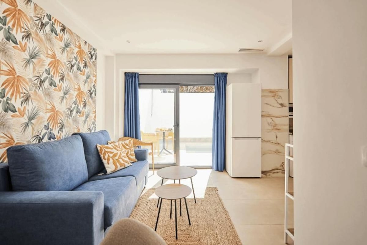 A living room with a sofa, a small table, and a view through a glass door to an outdoor area.