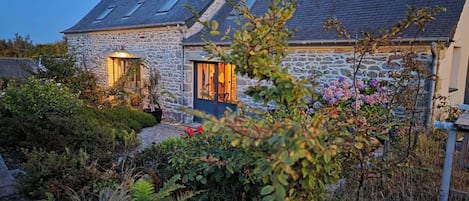 Una casa de piedra con techo inclinado y un jardín delantero.