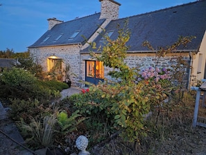 Ein Haus aus Stein mit einem geneigten Dach und einem Garten davor.