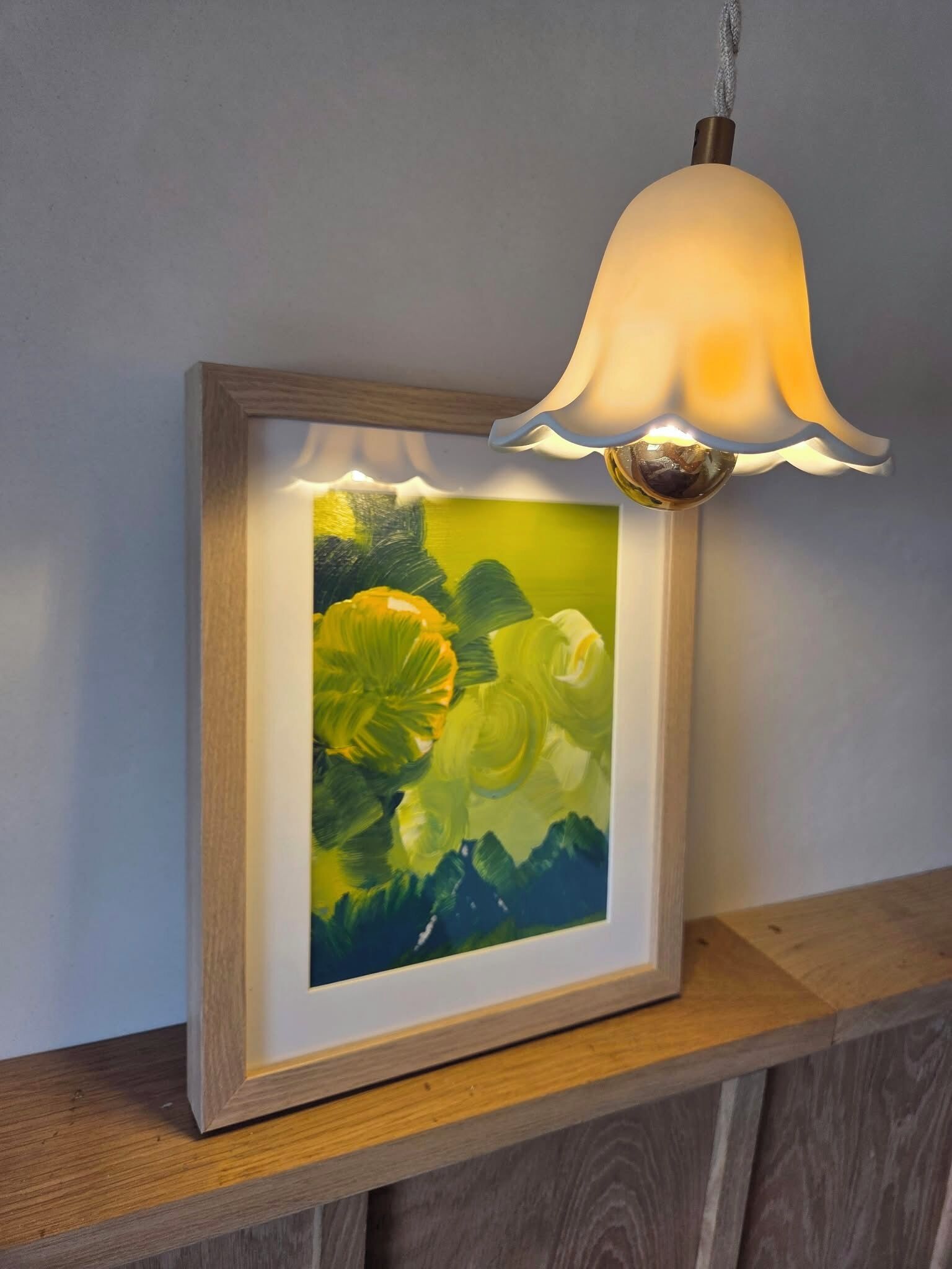 A framed painting with a hanging lamp above it.
