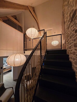Eine Treppe mit hölzernem Geländer, einer Steinwand und hängenden Papierlampen.