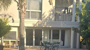 Un edificio de dos plantas con piscina, mobiliario exterior y una palmera.