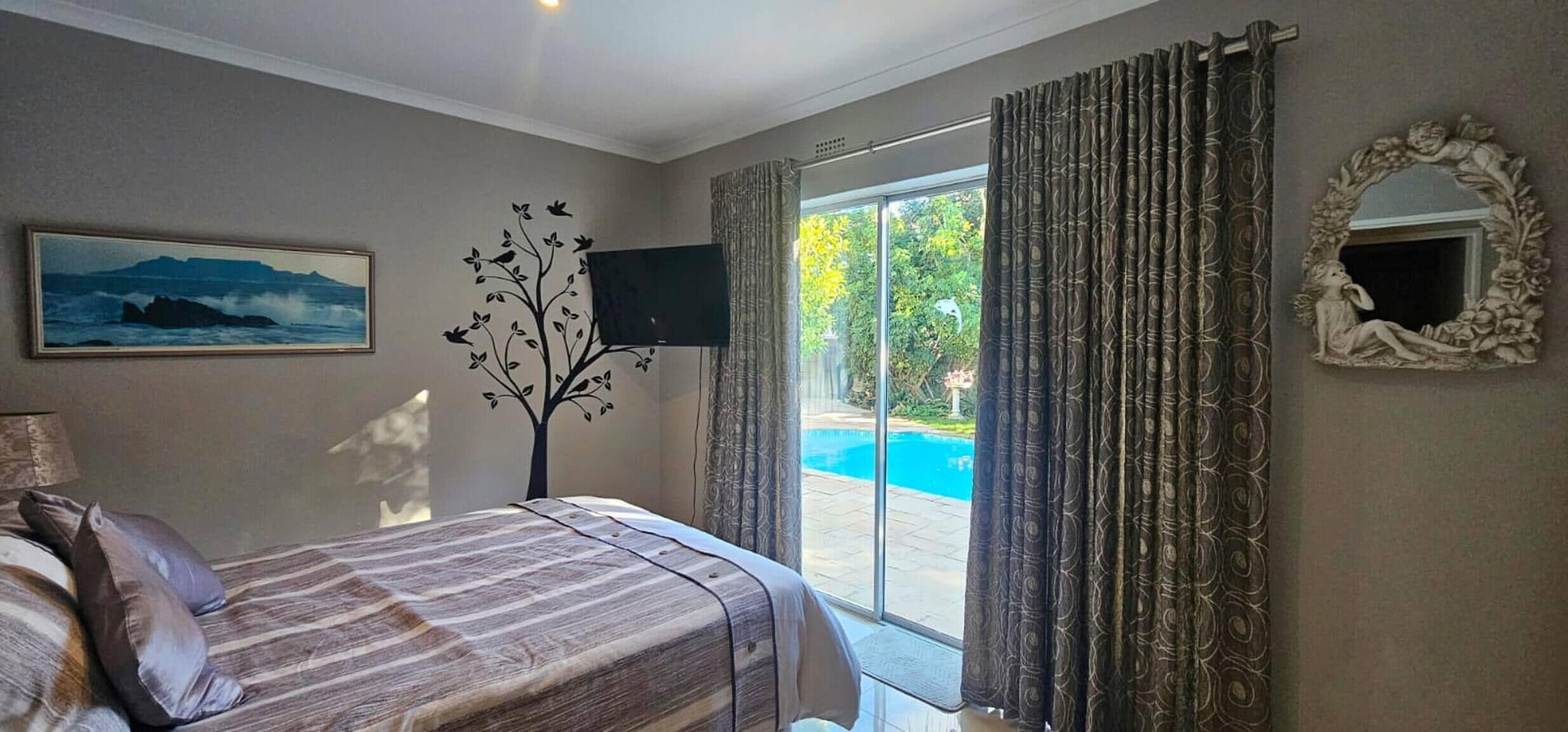 Un dormitorio con una cama, televisión, un cuadro y vistas a una piscina.