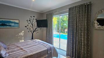 Un dormitorio con una cama, televisión, un cuadro y vistas a una piscina.