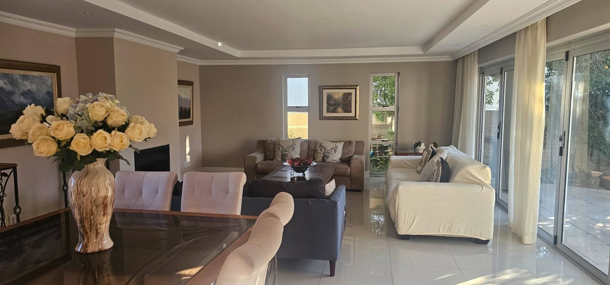 A spacious living room with a glass coffee table, two sofas, and a dining area with a vase of flowers.