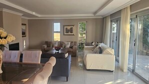Un salón espacioso con una mesa de centro de vidrio, dos sofás y una zona de comedor con un florero.