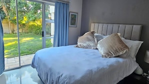 Un dormitorio con una cama grande, una mesita de noche, una lámpara y vistas a un jardín a través de una puerta corrediza.