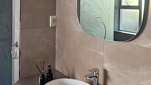 Un baño con un espejo redondo, un lavabo y una zona de ducha.