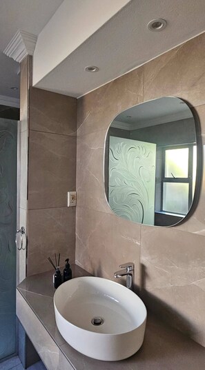 A bathroom with a round mirror, a sink, and a shower area. - Large Luxury Family Home in Upmarket Suburb (Cape Town)