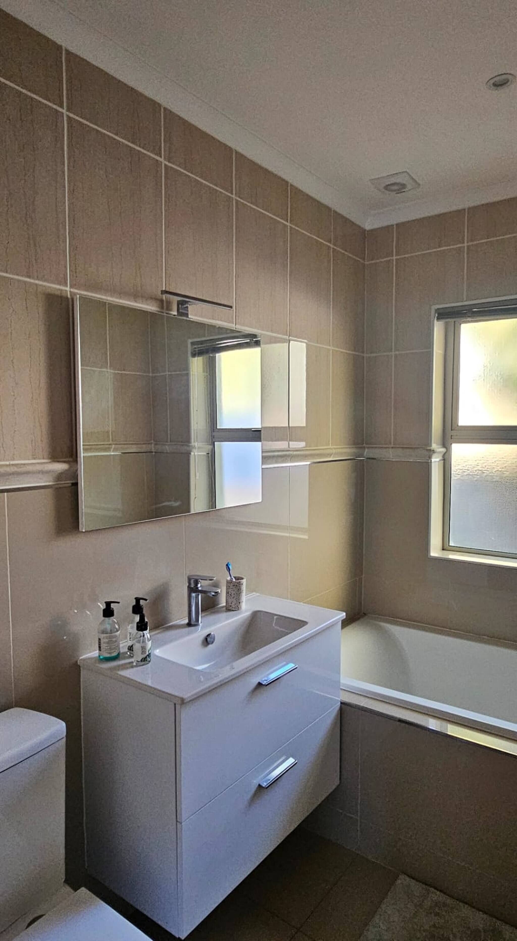 A modern bathroom with a white vanity, a bathtub, and a large mirror.