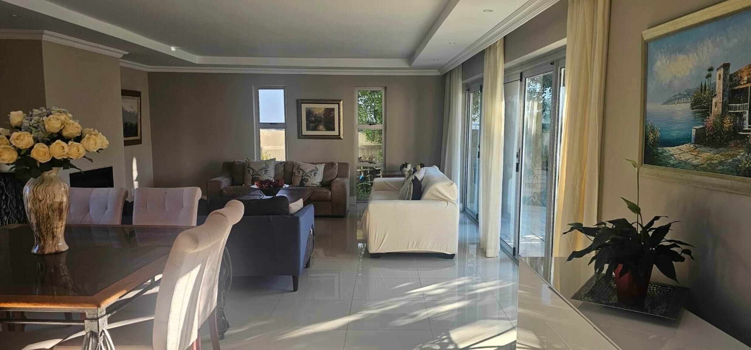 A spacious living area with a dining table, sofas, and a large window offering a view of the outdoors.