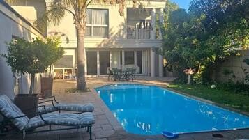 Un patio trasero residencial con piscina, muebles de patio y una zona de estar cubierta al aire libre.