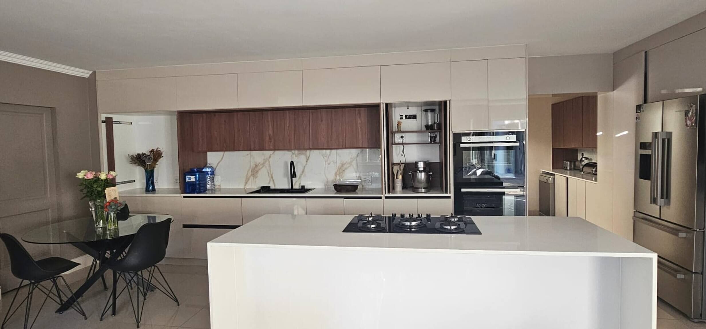 A modern kitchen with a central island, stainless steel appliances, and a dining area with a glass table and chairs.