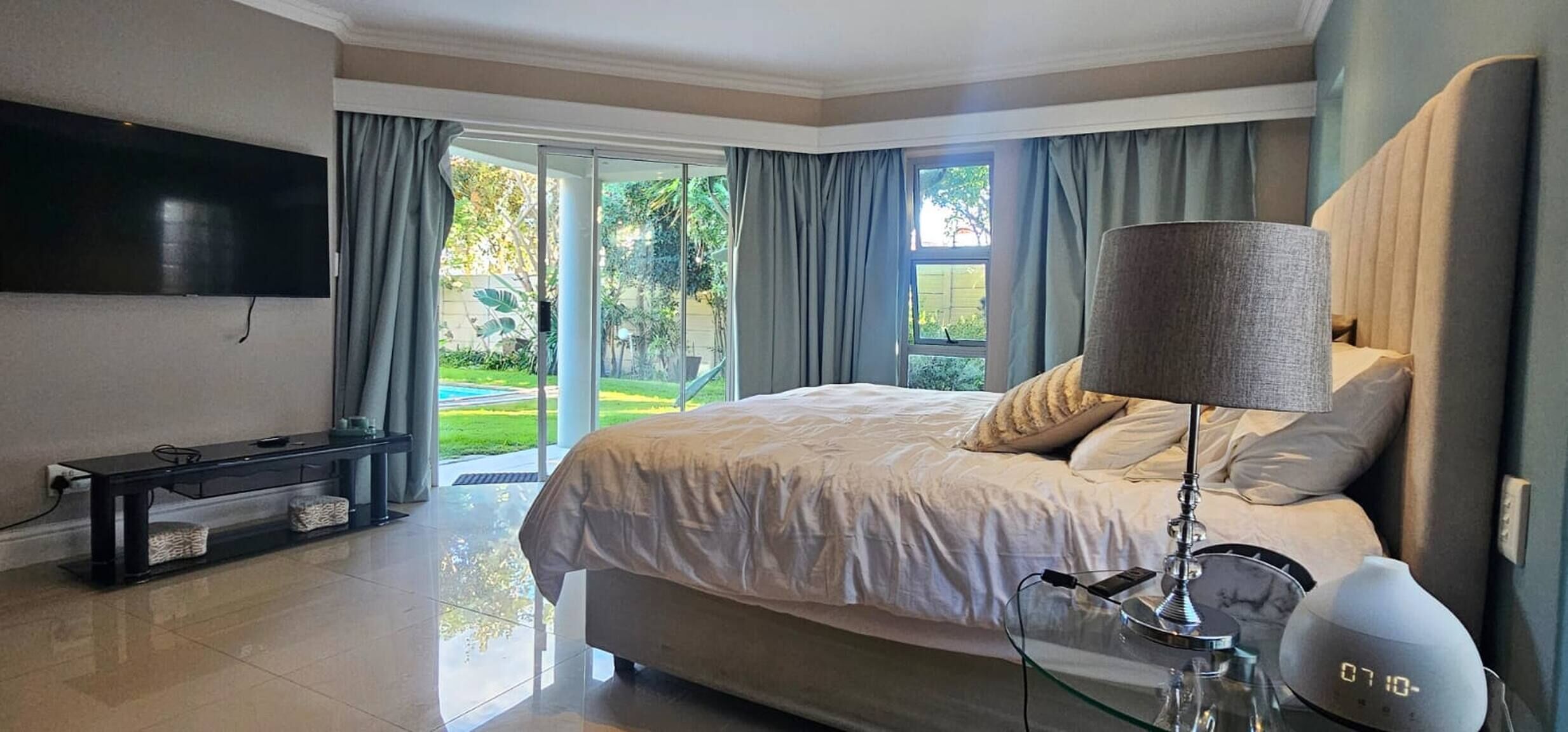 A hotel bedroom with a bed, a TV, a bedside table, and a lamp.