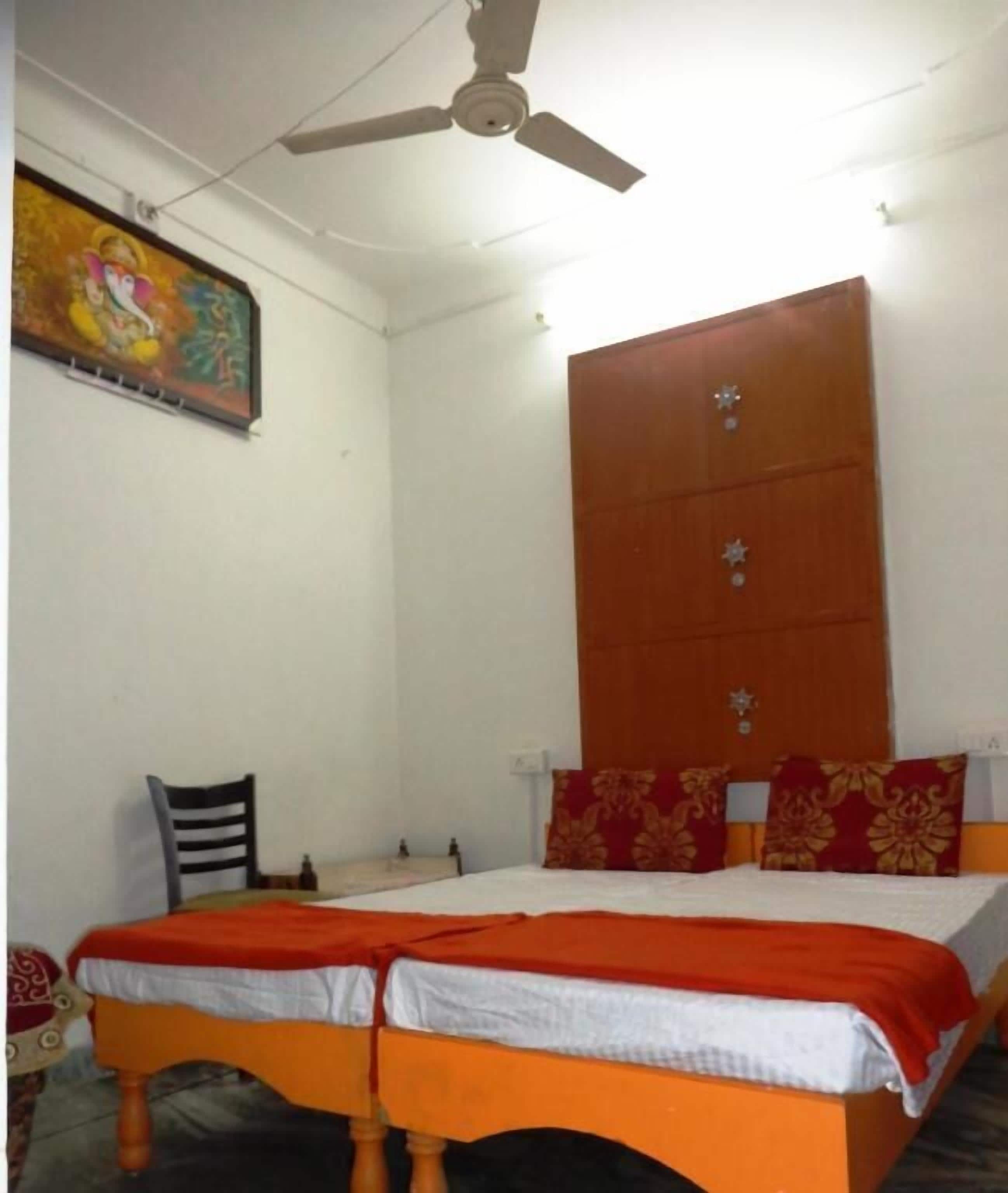 A bedroom with a bed, a ceiling fan, a wooden wardrobe, and a wall-mounted painting.