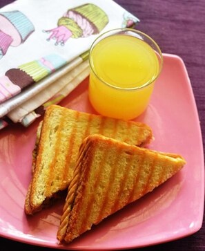 A pink plate with two grilled sandwiches and a glass of orange juice. - Mohan Villa Guest House (Udaipur)