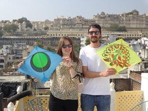 Two people holding kites on a rooftop with a view of a historic building in the background. - Mohan Villa Guest House (Udaipur)