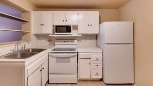 A compact kitchen with white cabinetry, a microwave, a stove, a sink, and a refrigerator. - Tampa Group Escape: 3 Units Near Downtown (Tampa)