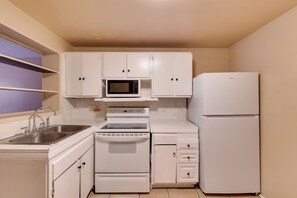 A compact kitchen with white cabinetry, a microwave, a stove, a sink, and a refrigerator. - Tampa Group Escape: 3 Units Near Downtown (Tampa)