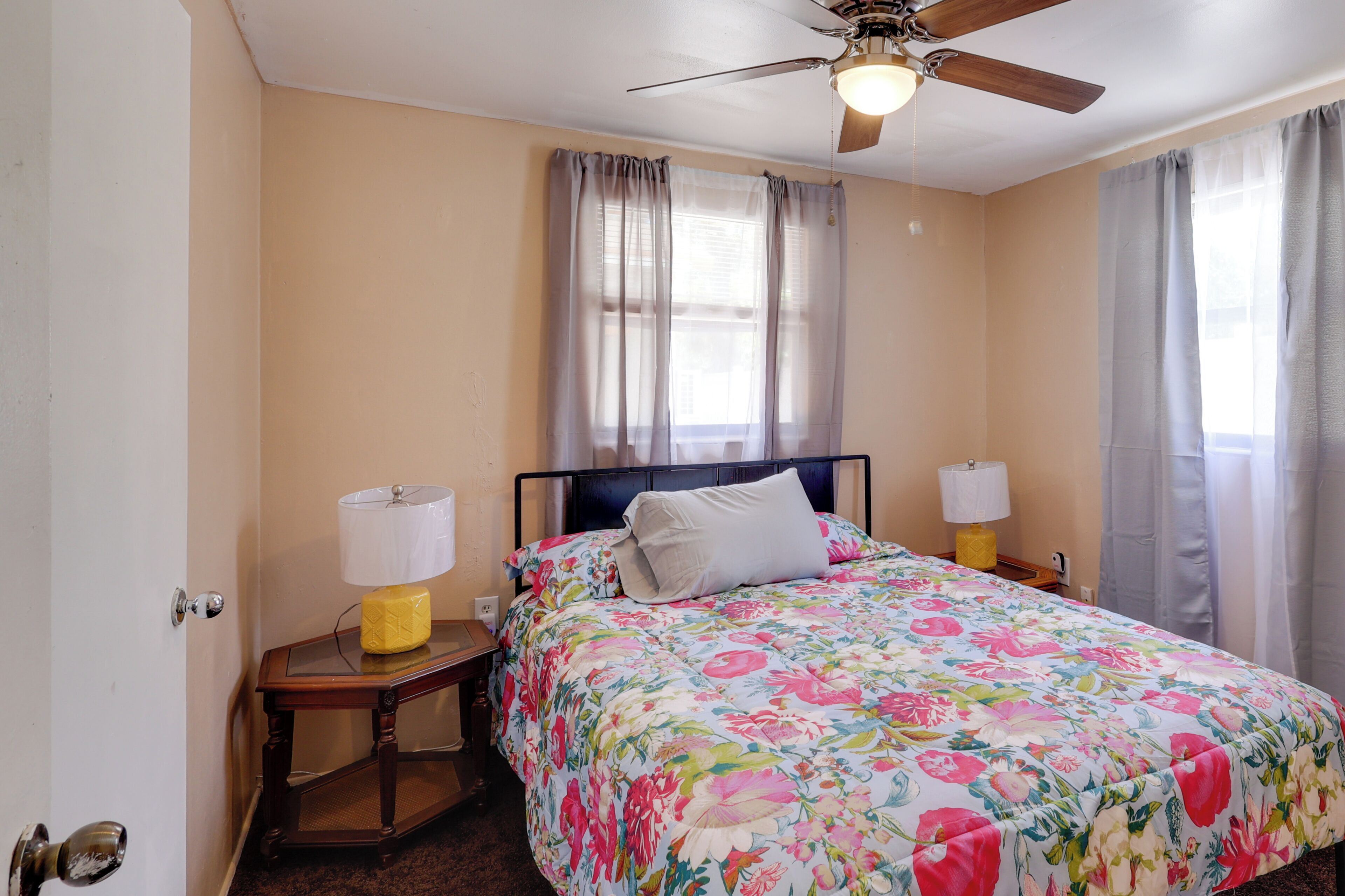 A bedroom with a bed, two bedside lamps, a ceiling fan, and a window with curtains.