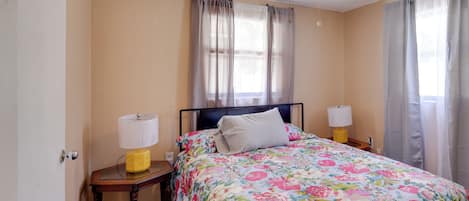 A bedroom with a bed, two bedside lamps, a ceiling fan, and a window with curtains.