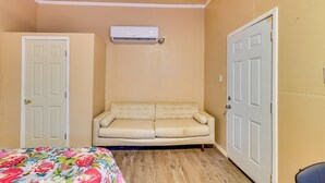 A room with a beige sofa, a floral bedspread, and an air conditioning unit mounted on the wall. - Tampa Group Escape: 3 Units Near Downtown (Tampa)