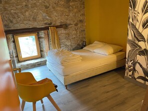 A room with a bed, a yellow chair, a stone wall, and a window.
