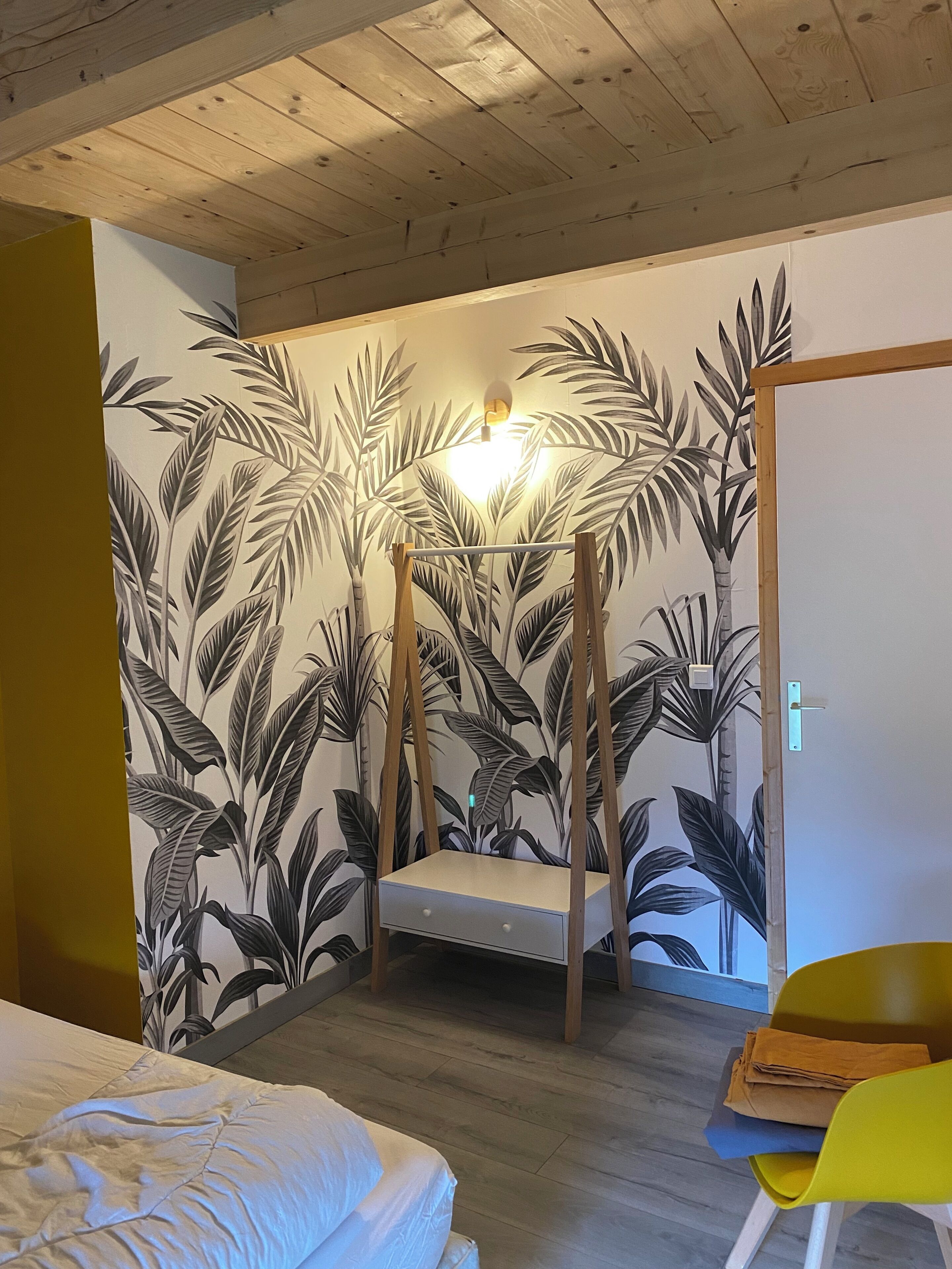 Une pièce comprenant un lit, une petite table, une chaise et un mur orné d’un motif de feuilles.