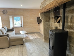 A cozy living room with a stone fireplace, a sofa, a small table, and a clock on the wall.