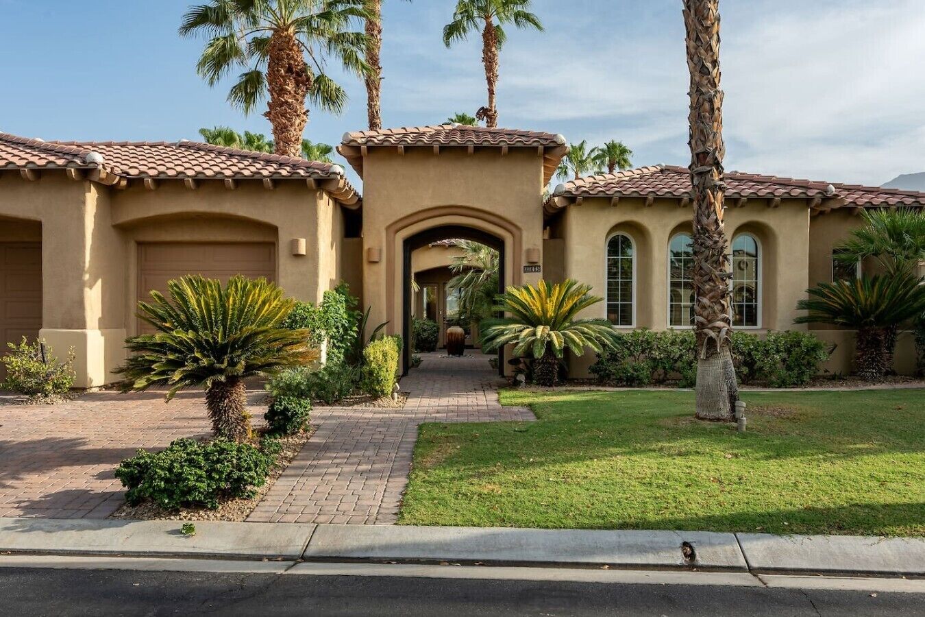 A two-story building with a tiled roof, a central archway, and a well-maintained lawn with palm trees.