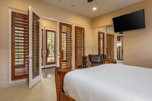 A bedroom with a large bed, wooden doors with louvered windows, a television mounted on the wall, and a chair. - Canyon House at PGA West | Poolside Golf Views (La Quinta)