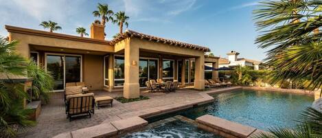 A residential property with a swimming pool, outdoor seating, and palm trees.