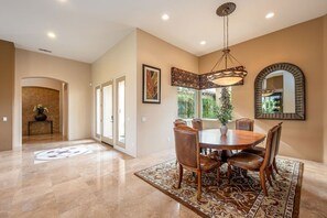 A spacious dining area with a round table, chairs, and a chandelier. - Canyon House at PGA West | Poolside Golf Views (La Quinta)