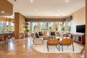 A spacious living room with a large sofa, leather chairs, a coffee table, and a TV. - Canyon House at PGA West | Poolside Golf Views (La Quinta)