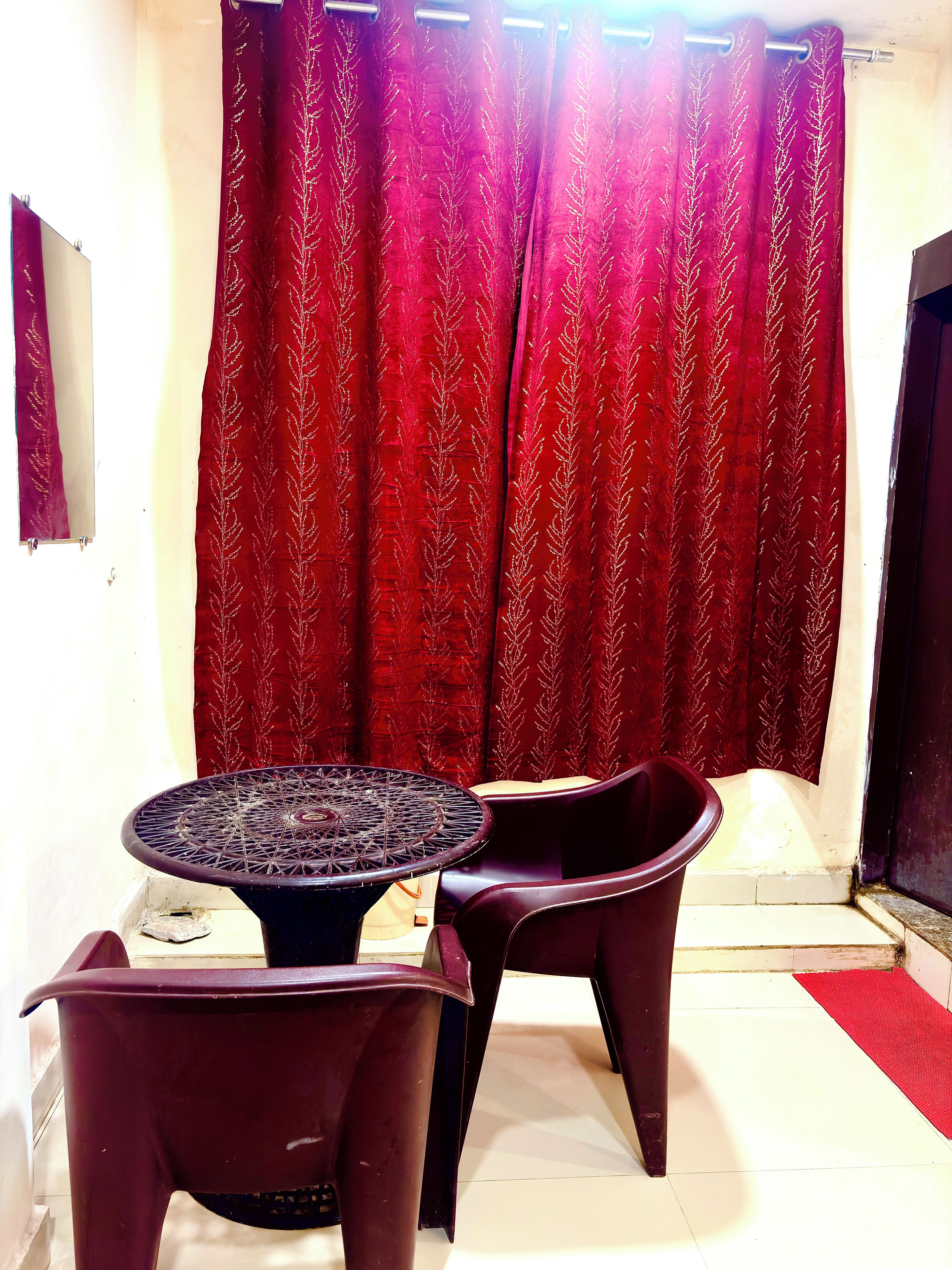 A room with a round table and two chairs, a red curtain with a leaf pattern, and a red doormat.
