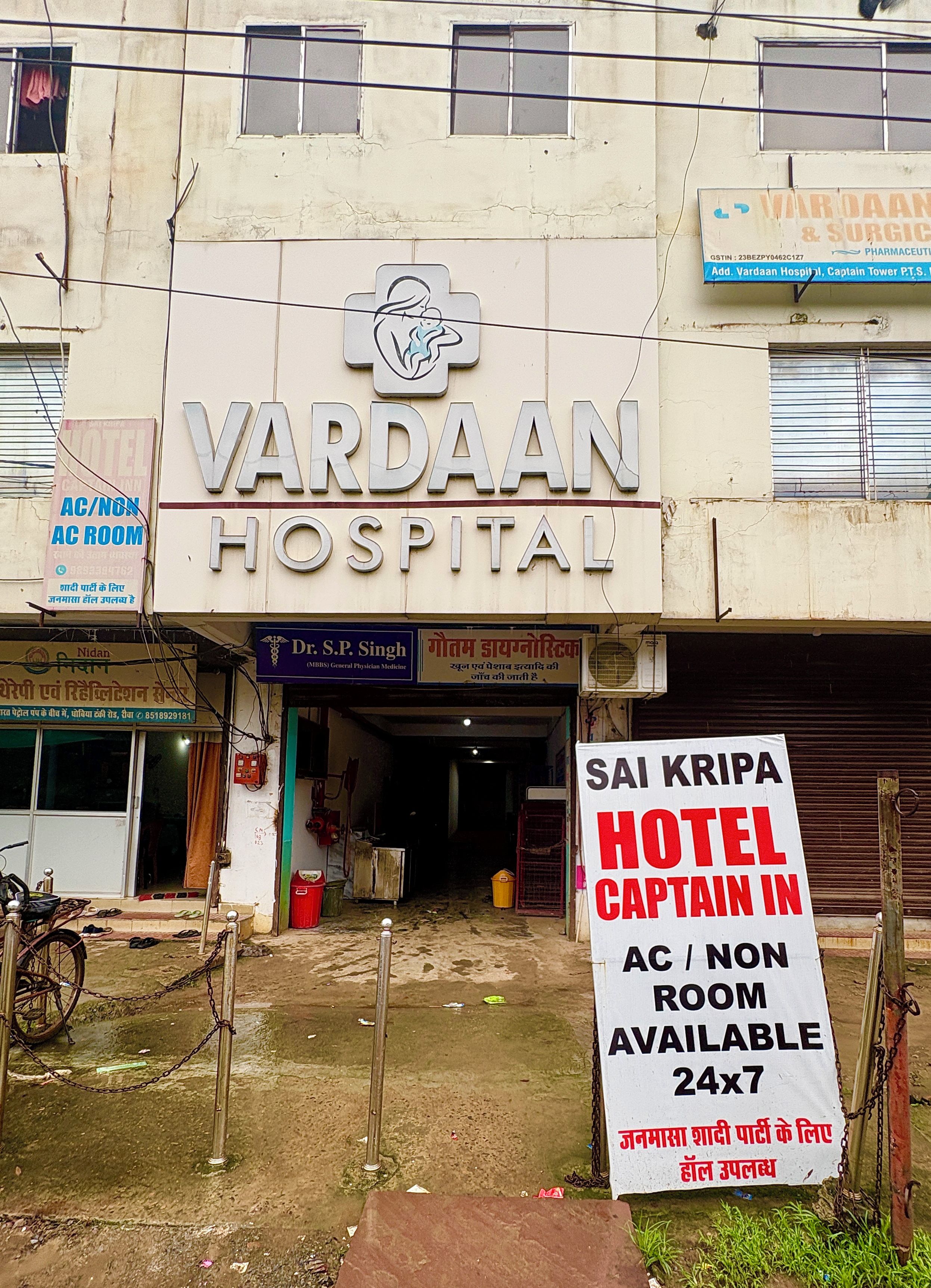 A building with a sign for Vardaam Hospital and a sign for a hotel named Sai Kripa.