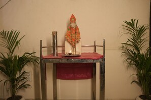 A table with a statue, a metal container, and a lit candle. There are two potted plants on either side of the table.