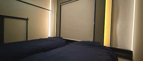 A room with two beds aligned against a wall, a door, and a window with a light fixture above.