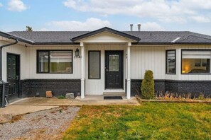 Une maison de plain-pied avec un porche à l’avant, une porte noire et un petit jardin devant.