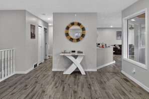 Un couloir avec une console blanche, un miroir rond doté d’un cadre noir et doré, et un escalier avec des balustres blanches.