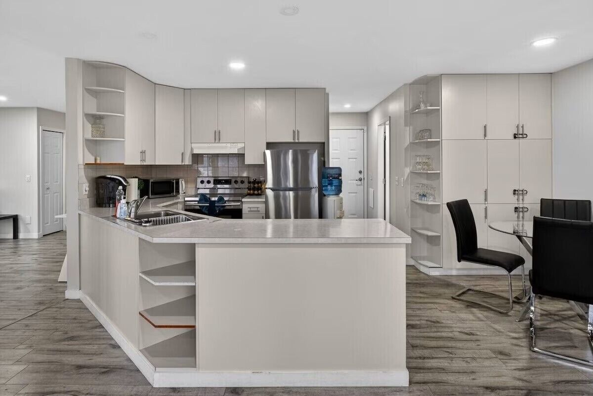 Una cocina moderna con armarios blancos, una isla central y un comedor con mesa de vidrio y sillas negras.