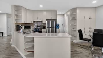 Una cocina moderna con armarios blancos, una isla central y un comedor con mesa de vidrio y sillas negras.