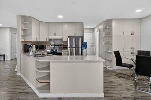 Une cuisine moderne avec des meubles blancs, un îlot central et un coin repas comprenant une table en verre et des chaises noires.