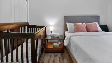 Un dormitorio con una cuna, una mesita de noche con lámpara y una cama con almohadas.